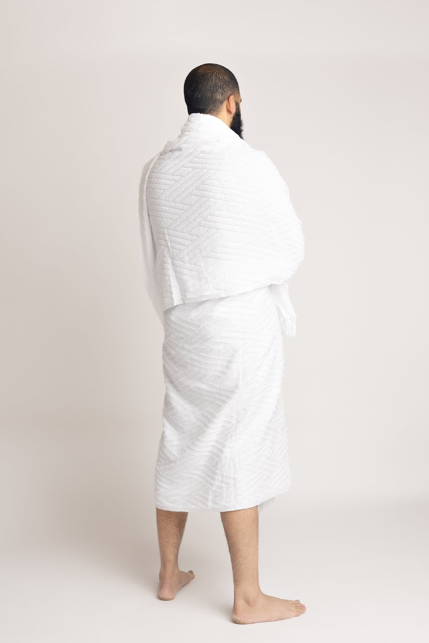 A 3/4 back pose photo of a muslim man wearing a two piece mens white ihram set from the halal caravan